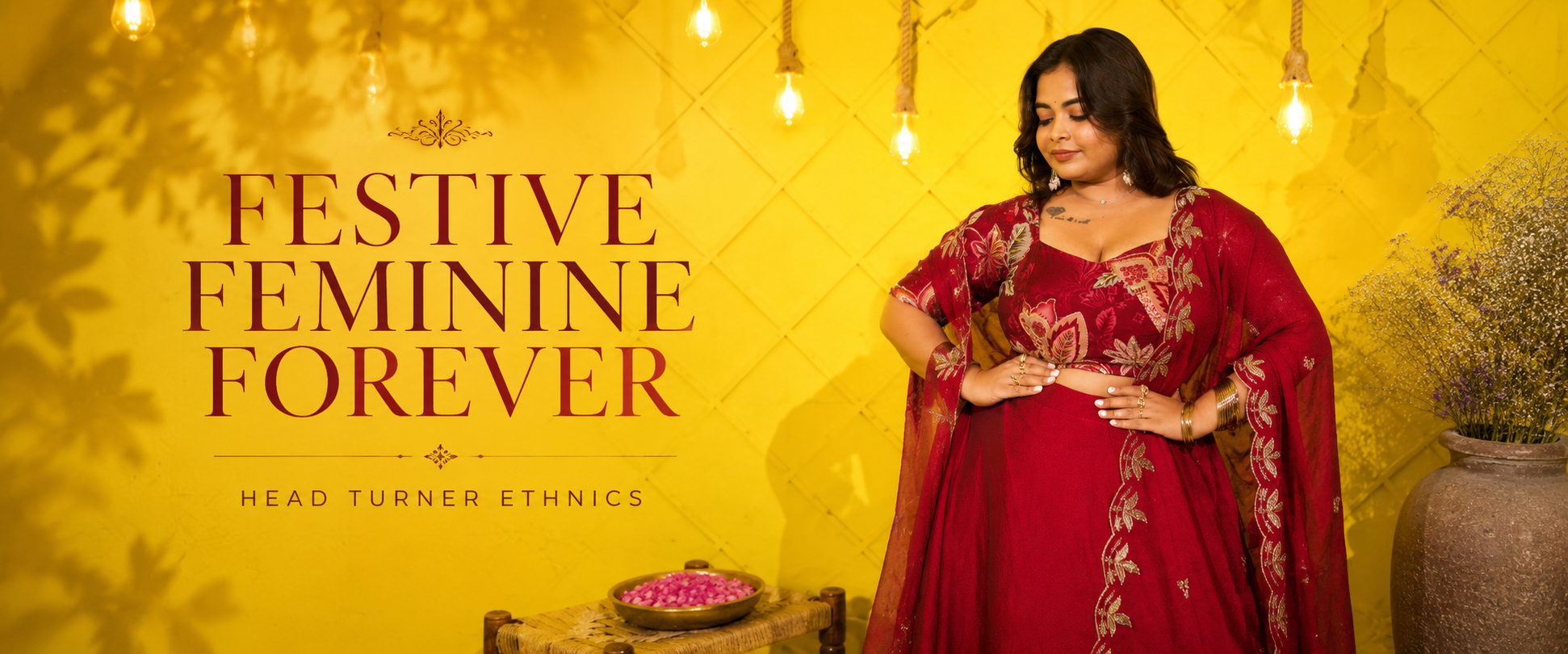 A woman wearing a red embroidered traditional outfit stands against a yellow wall with hanging lights and decorative text that reads 'Festive Feminine Forever' and 'Head Turner Ethnics'.
